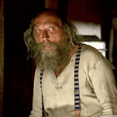 a man with a beard and suspenders has a picture of him on the website thefuckingenius.com
