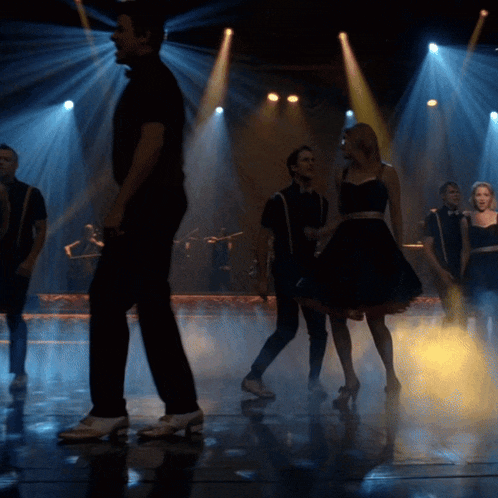 a group of people are dancing on a stage with spotlights