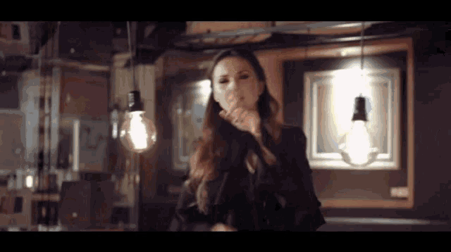 a woman blowing a kiss in a dark room with a light bulb hanging from the ceiling