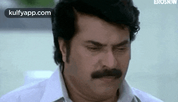 a man with a mustache and a white shirt is looking down .