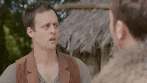 a man is talking to another man in front of a hut .