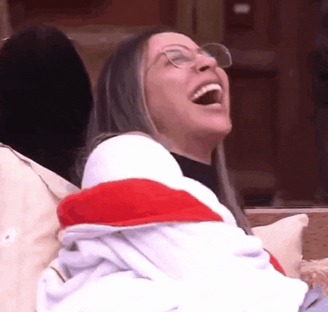 a woman wearing glasses is sitting on a couch and laughing .