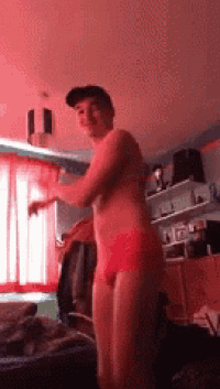 a shirtless man in red underwear is standing in a room with red curtains .