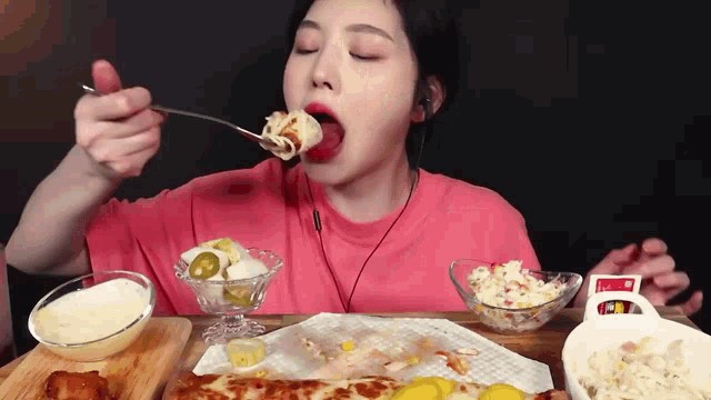 a woman in a pink shirt is eating a pizza