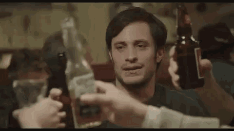 a man is holding a bottle of beer and a bottle of tequila while a group of people toast him .