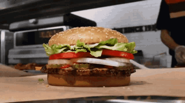a hamburger with lettuce tomato and onions sits on a piece of paper