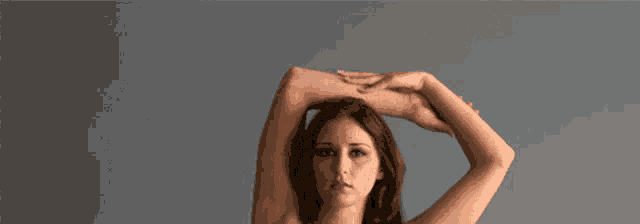a woman stretches her arms over her head against a gray background