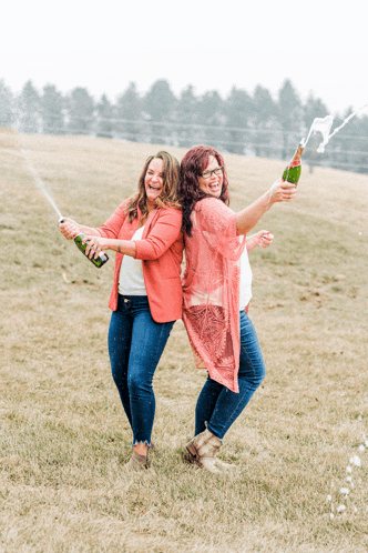 two women are standing in a field holding champagne bottles