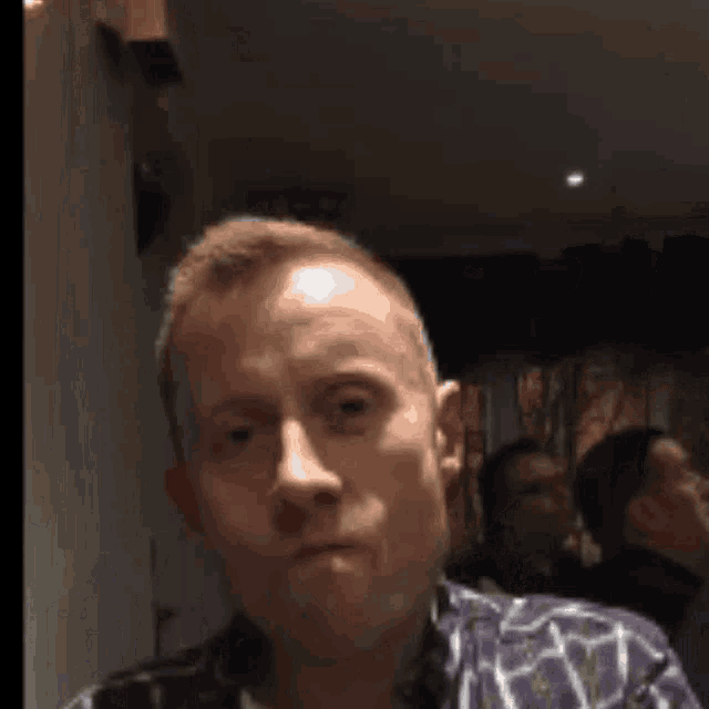 a man in a plaid shirt is taking a selfie in a dark room .