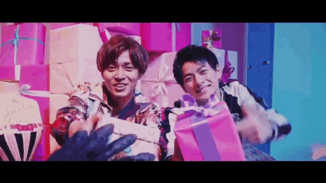 two young men are standing next to each other holding pink gifts .