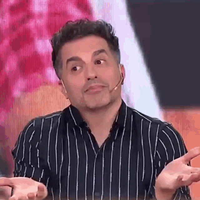 a man in a striped shirt is making a funny face with his hands out .