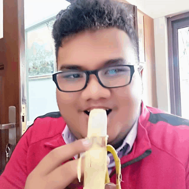 a man wearing glasses is eating a banana in front of a door
