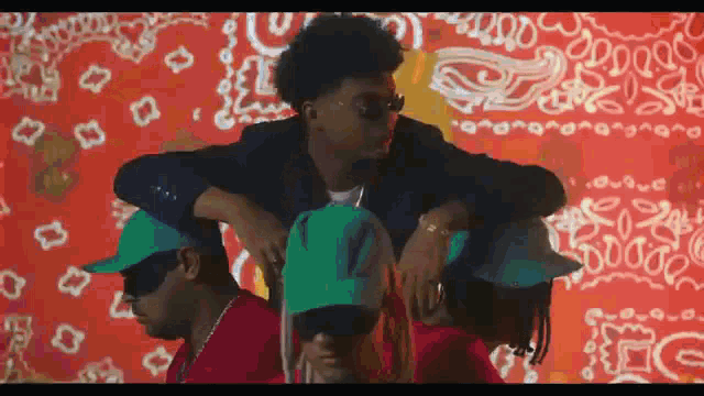 a group of men wearing green hats and sunglasses are standing in front of a red bandana .