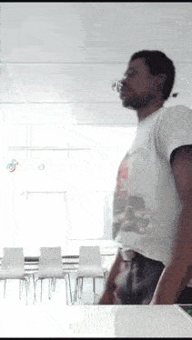 a man in a white t-shirt is standing in a room with chairs
