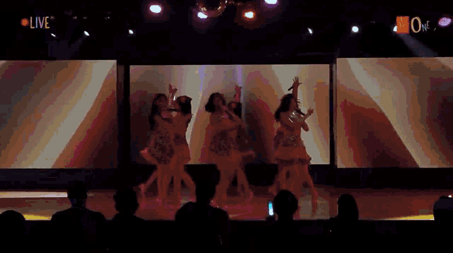 a group of women singing on a stage with the words live on the bottom right
