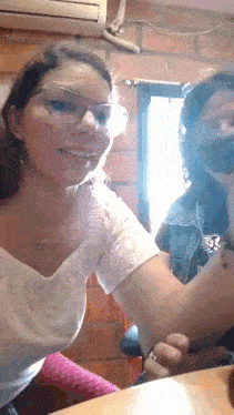 a woman wearing glasses and a white shirt is sitting next to another woman .