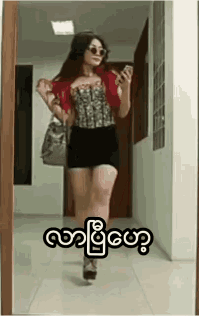a woman is walking down a hallway while holding a cell phone and a purse