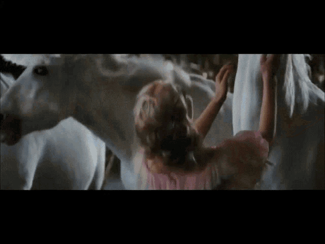 a little girl in a pink dress is touching a white horse