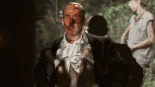 a man in a suit with blood on his face is standing in a dark room