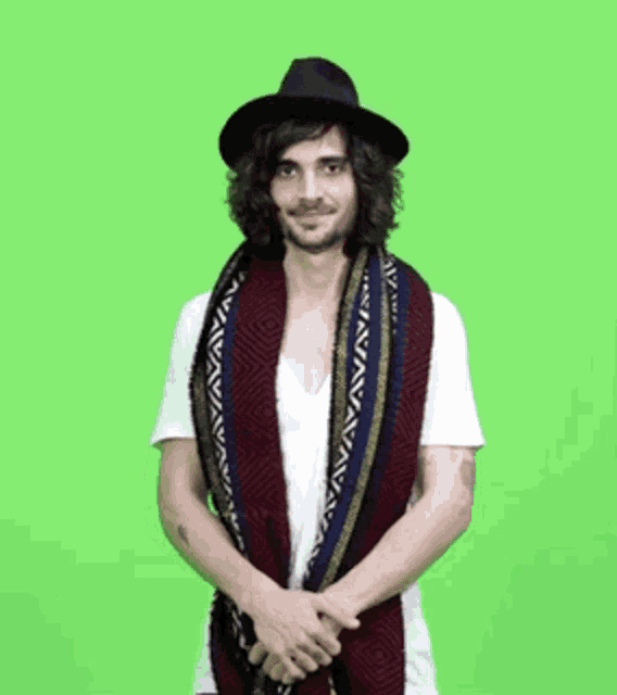 a man wearing a hat and a scarf is standing in front of a green background