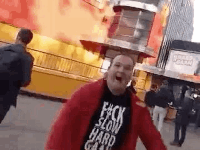 a man wearing a red jacket and a black shirt is standing in front of a carnival ride .