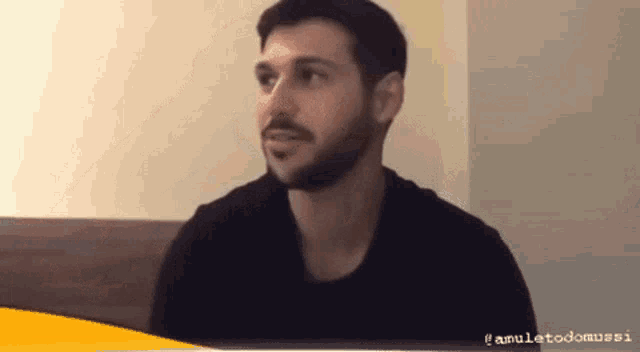 a man with a beard wearing a black shirt is sitting in a room .