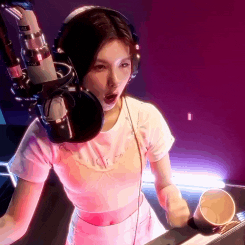 a woman wearing headphones is singing into a microphone and holding a cup in her hand