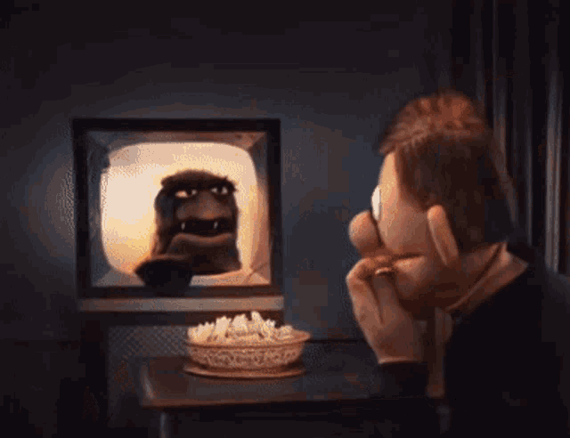 a man watches a cartoon on a television with a bowl of popcorn in front of him