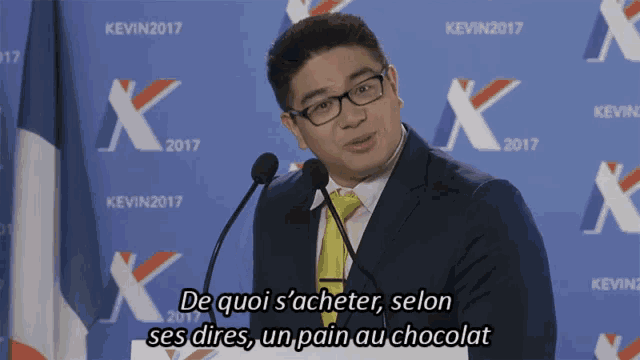 a man in a suit and tie is giving a speech in front of a kevin2017 sign