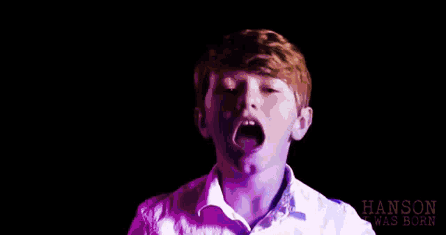 a young boy in a white shirt is singing into a microphone .