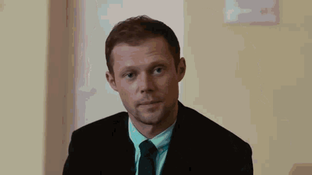 a man in a suit and tie is sitting in front of a yellow wall and looking at the camera .