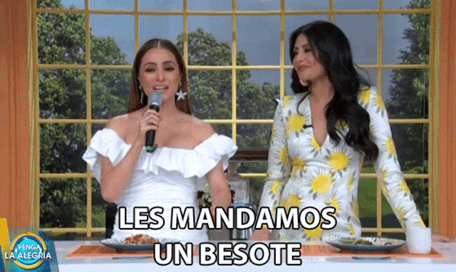 two women are sitting at a table with a microphone and the words les mandamos un besote