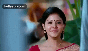 a woman is smiling and looking at the camera while wearing a red saree .