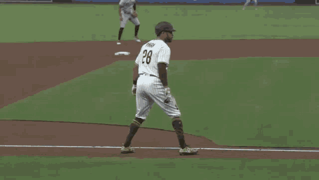a baseball player is walking towards the base while a pitcher watches .