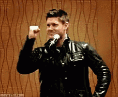 a man in a leather jacket is holding a microphone and giving a fist pump