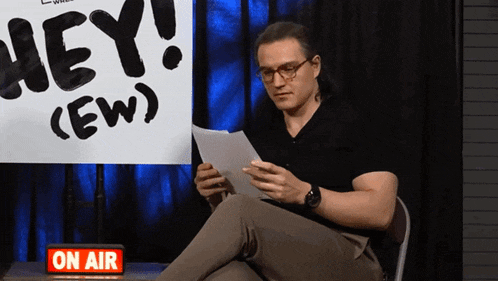 a man sitting in front of a sign that says hey ew