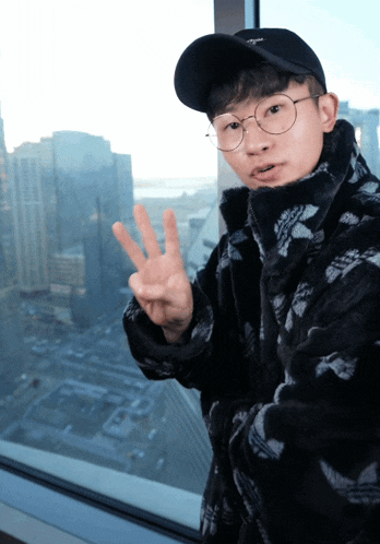 a young man wearing glasses and a black hat is giving a peace sign