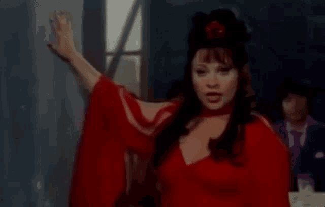 a woman in a red dress is standing in front of a blackboard and pointing at it .