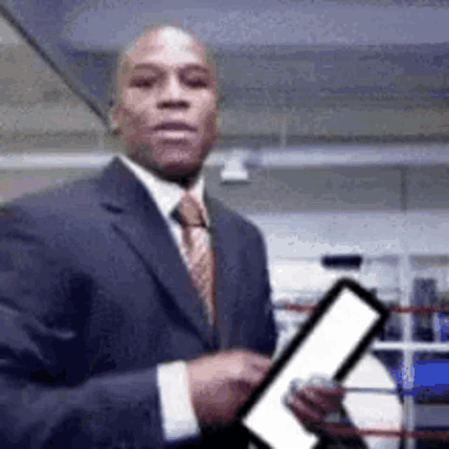 a man in a suit and tie is holding a tablet in front of a boxing ring