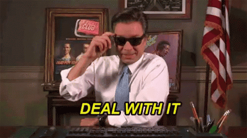 a man wearing sunglasses and a tie is sitting at a desk with the words deal with it above him .