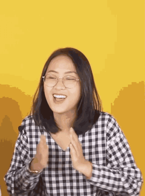 a woman wearing glasses and a plaid shirt is smiling and clapping