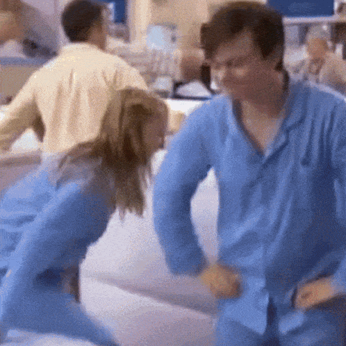 a man and a woman in blue pajamas are dancing on a couch .