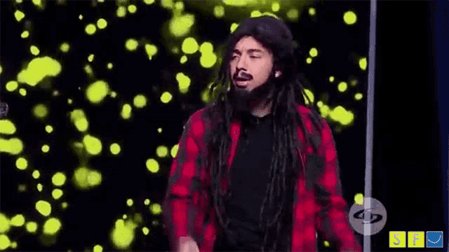 a man with dreadlocks and a beard is flexing his muscles in front of a green background .