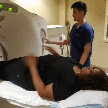 Mulher erguendo os braços ao entrar numa câmara de ressonância magnética.