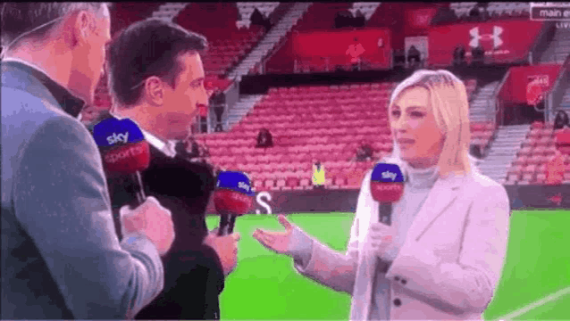 a woman is talking into a microphone on a soccer field with two men .
