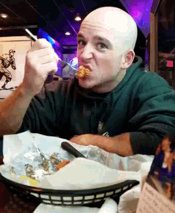 a man with a bald head is sitting at a table eating food with a fork