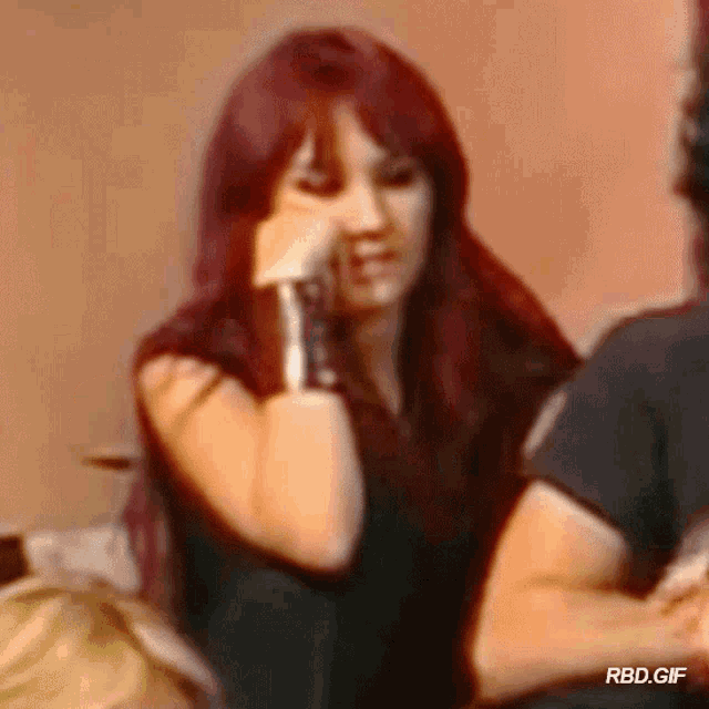 a woman with red hair is sitting on a couch with her hand on her chin .