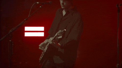 a man in a black shirt is playing a guitar in front of a microphone