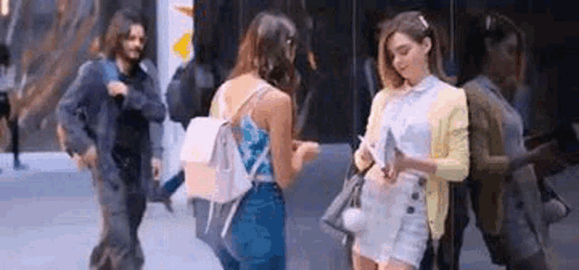 a man and two women are walking down a city street . one of the women is looking at her phone .