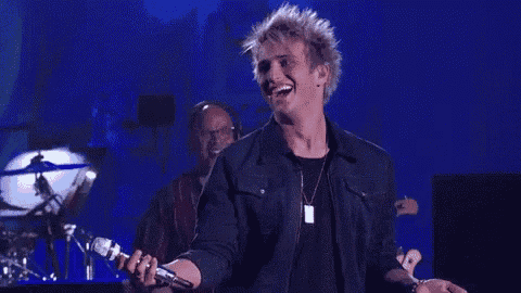 a man is singing into a microphone on a stage with a drummer in the background .